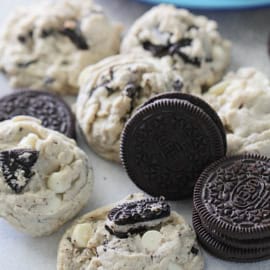 An assortment of cookies with chunks of chocolate and cream cookies, alongside whole chocolate and cream sandwich cookies on a light surface.