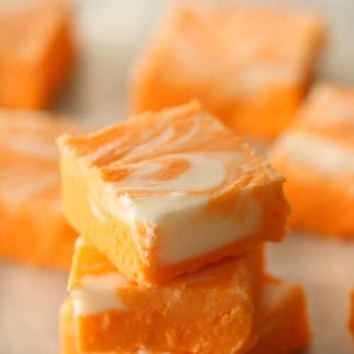 3 Orange Creamsicle Fudge pieces stacked on top of each other. Remaining fudge pieces in the background.