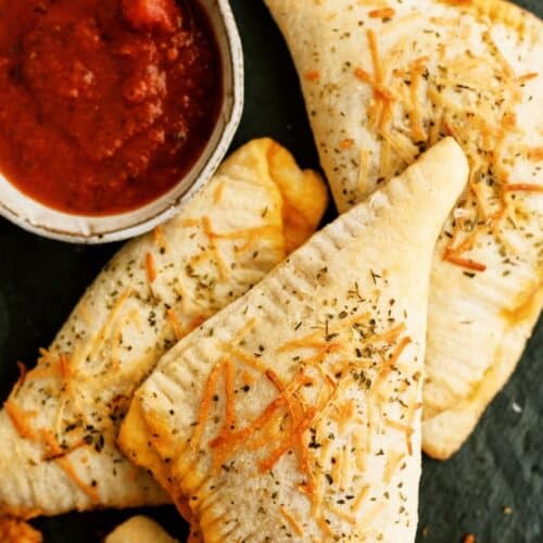 Top view of Crispy baked Calzones with a cup of sauce for dipping.