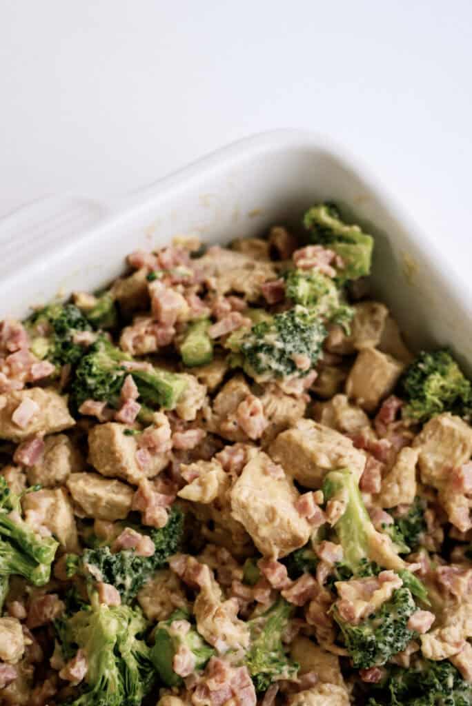 A casserole dish filled with a creamy mixture of diced chicken, broccoli florets, and small bits of ham.