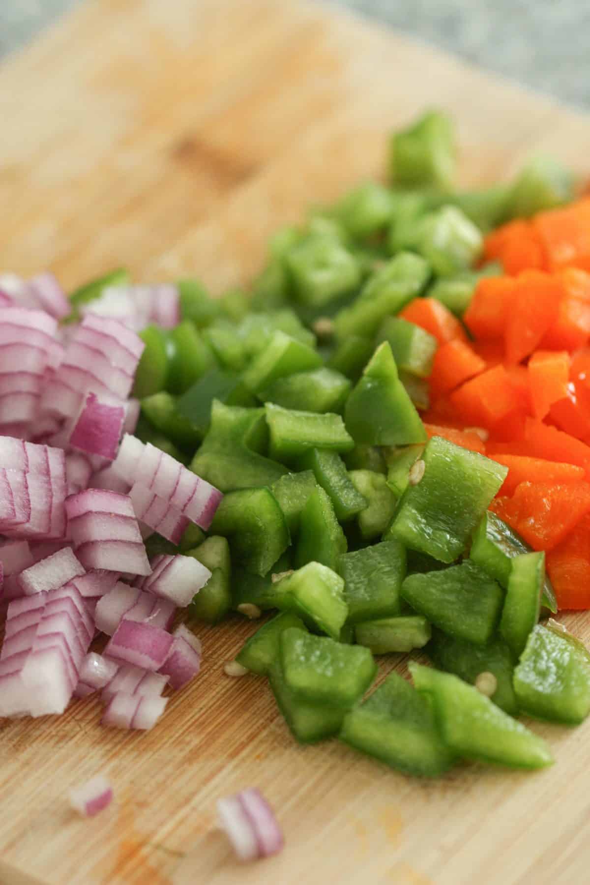 Chopped vegetables on a cutting board: diced red onion, green bell pepper, and red bell pepper.