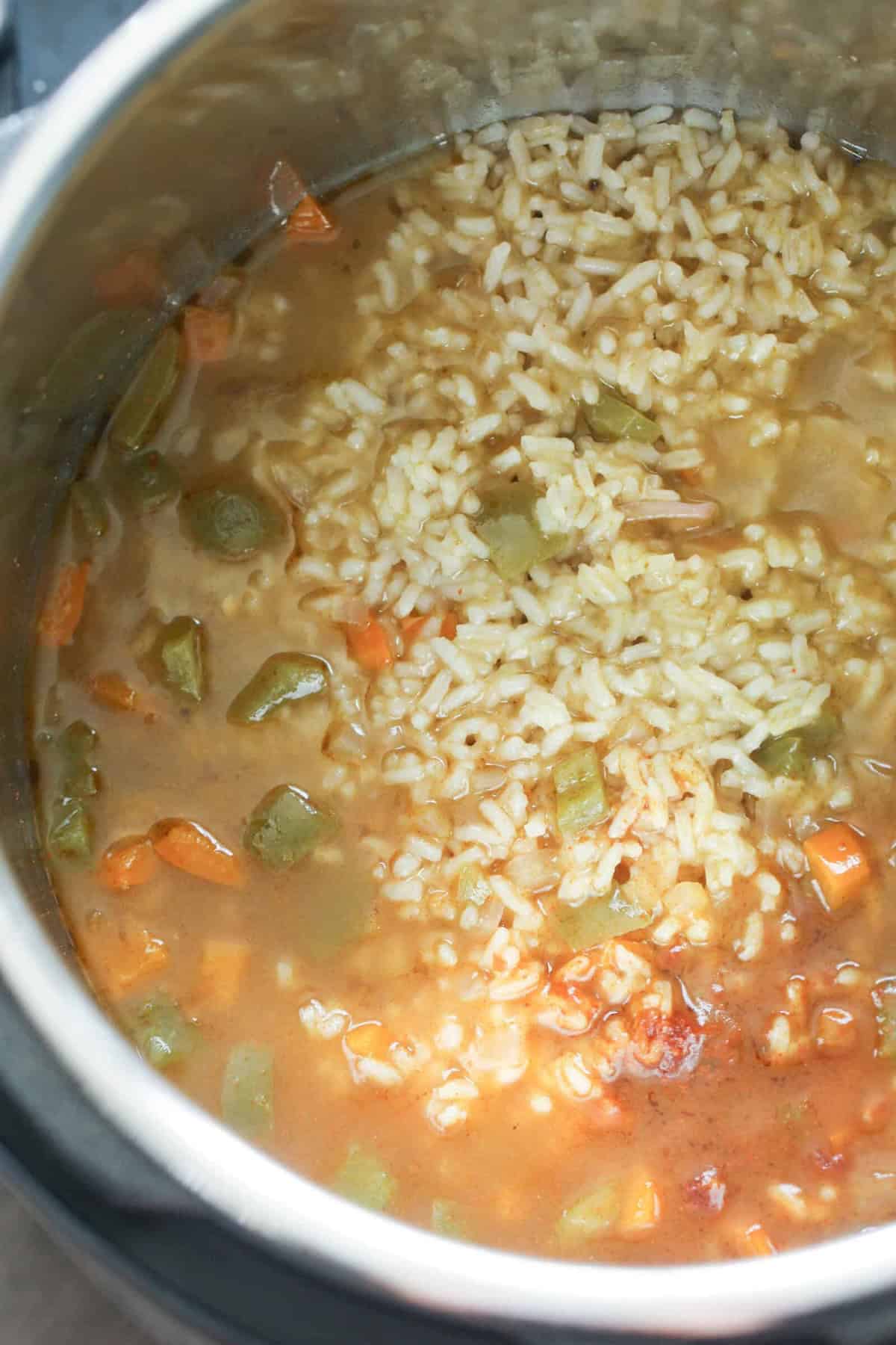 A pot filled with a cooked mixture of rice, diced carrots, green peppers, and a brown broth.