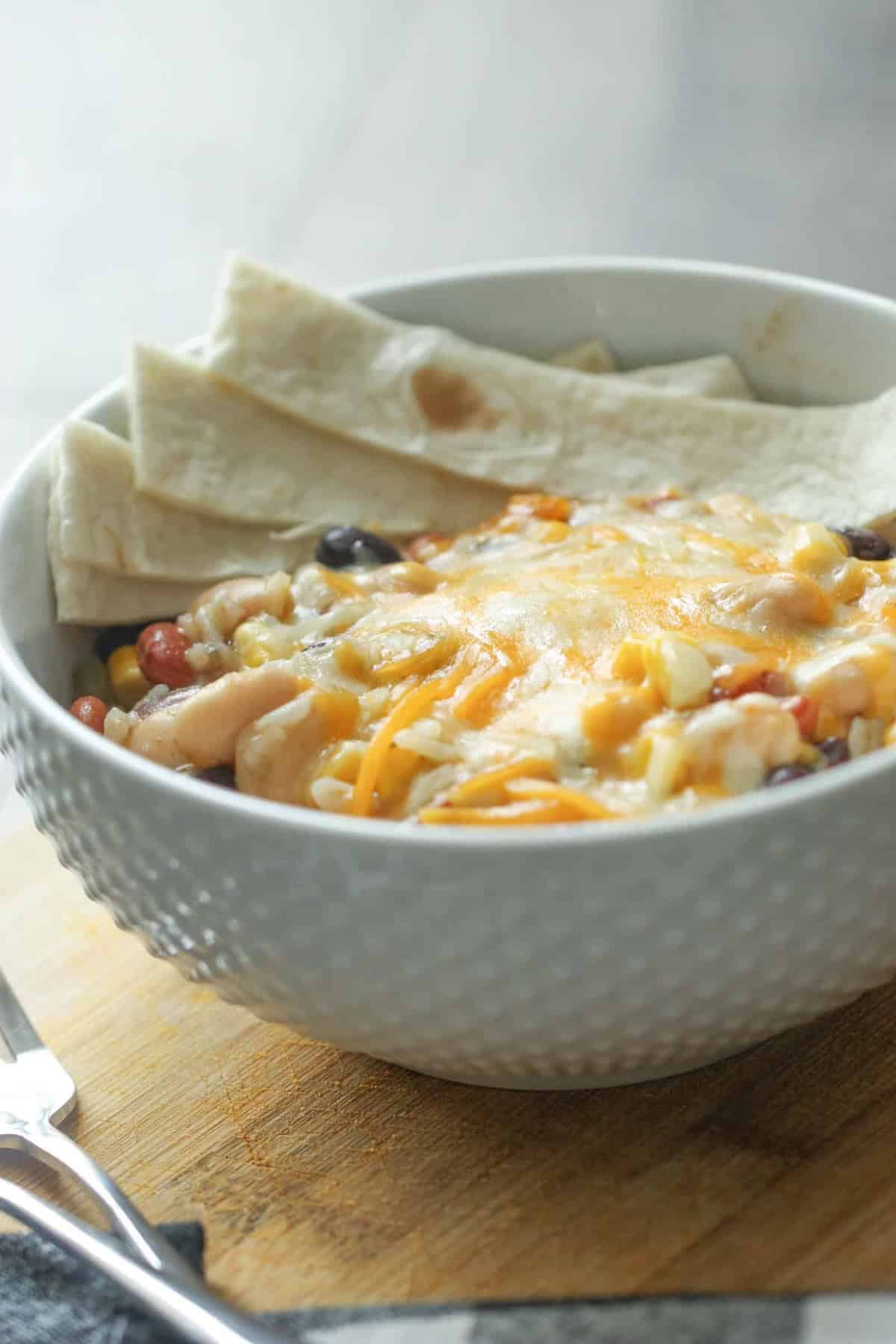 Bowl of three bean enchilada casserole topped with shredded cheese and garnished with tortilla strips.