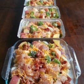 Four trays of assorted uncooked casserole ingredients, including diced meat, vegetables, and shredded cheese, are lined up on a wooden table.