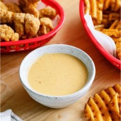 A bowl of Copycat Chick-Fil-A Sauce surrounded by a basket of chicken tenders and a basket of french fries.