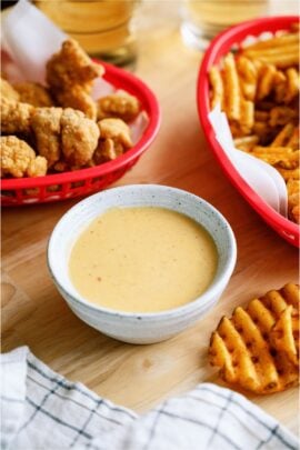 A bowl of Copycat Chick-Fil-A Sauce surrounded by a basket of chicken tenders and a basket of french fries.