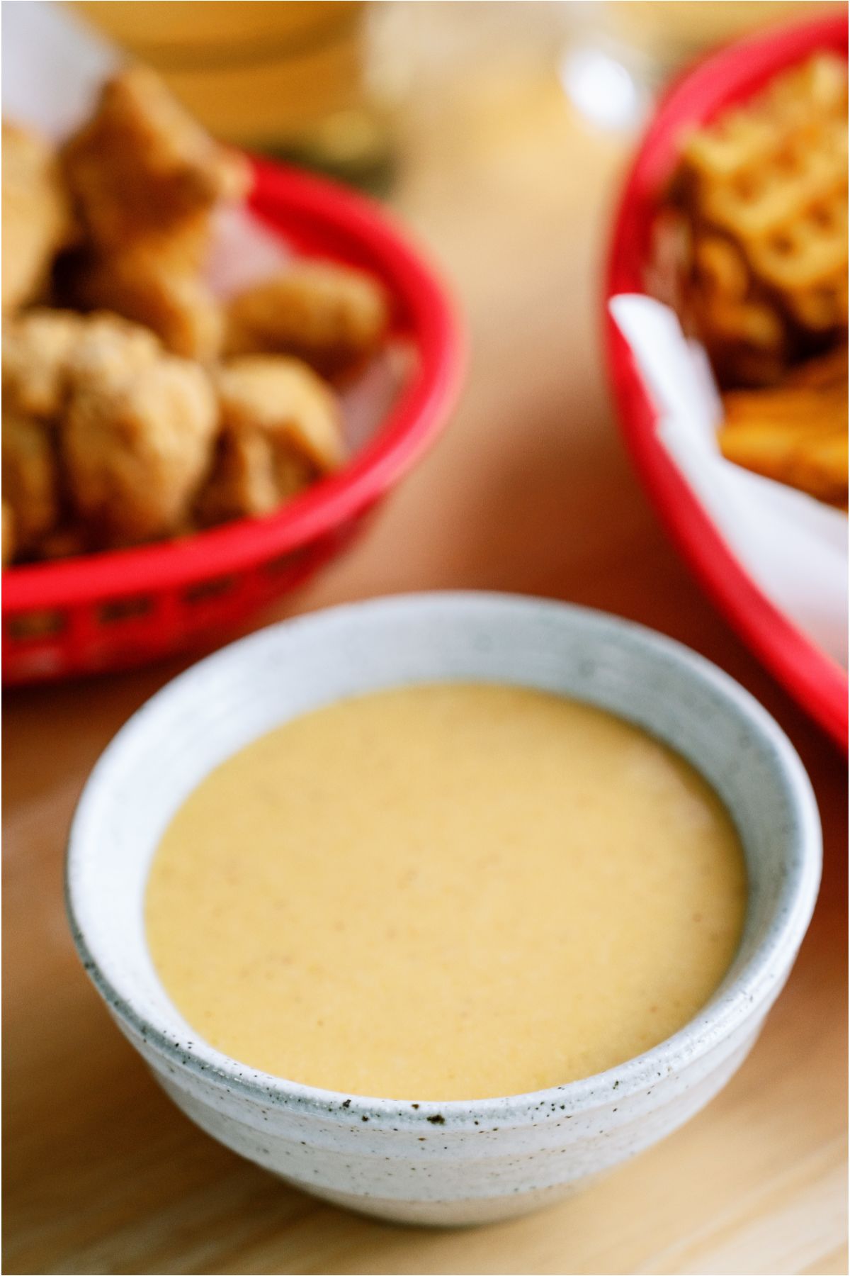 A large bowl of Copycat Chick-Fil-A Sauce with a basket of fries and a basket of chicken tenders on the side.