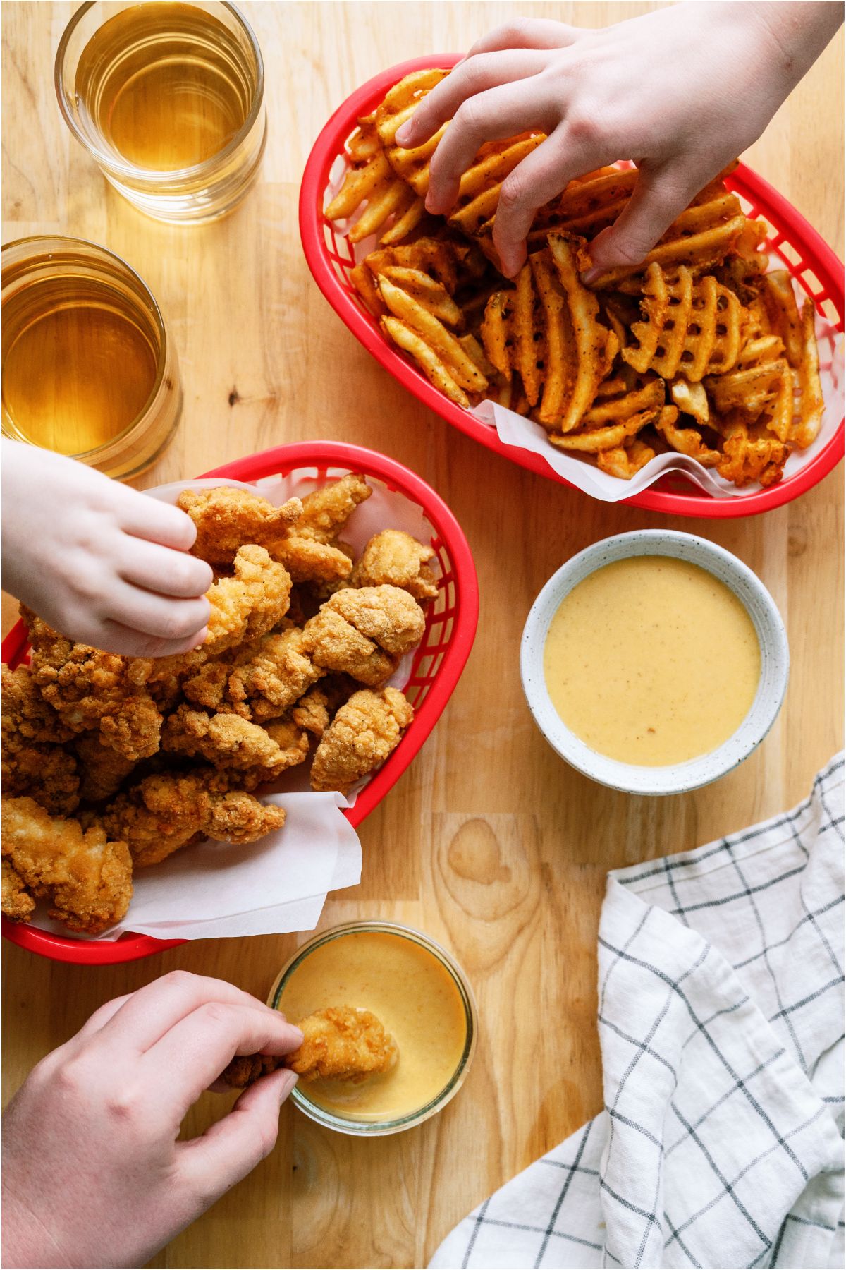 Several hands reaching in Chicken tender basket, french fries basket, and Copycat Chick-Fil-A Sauce bowl.