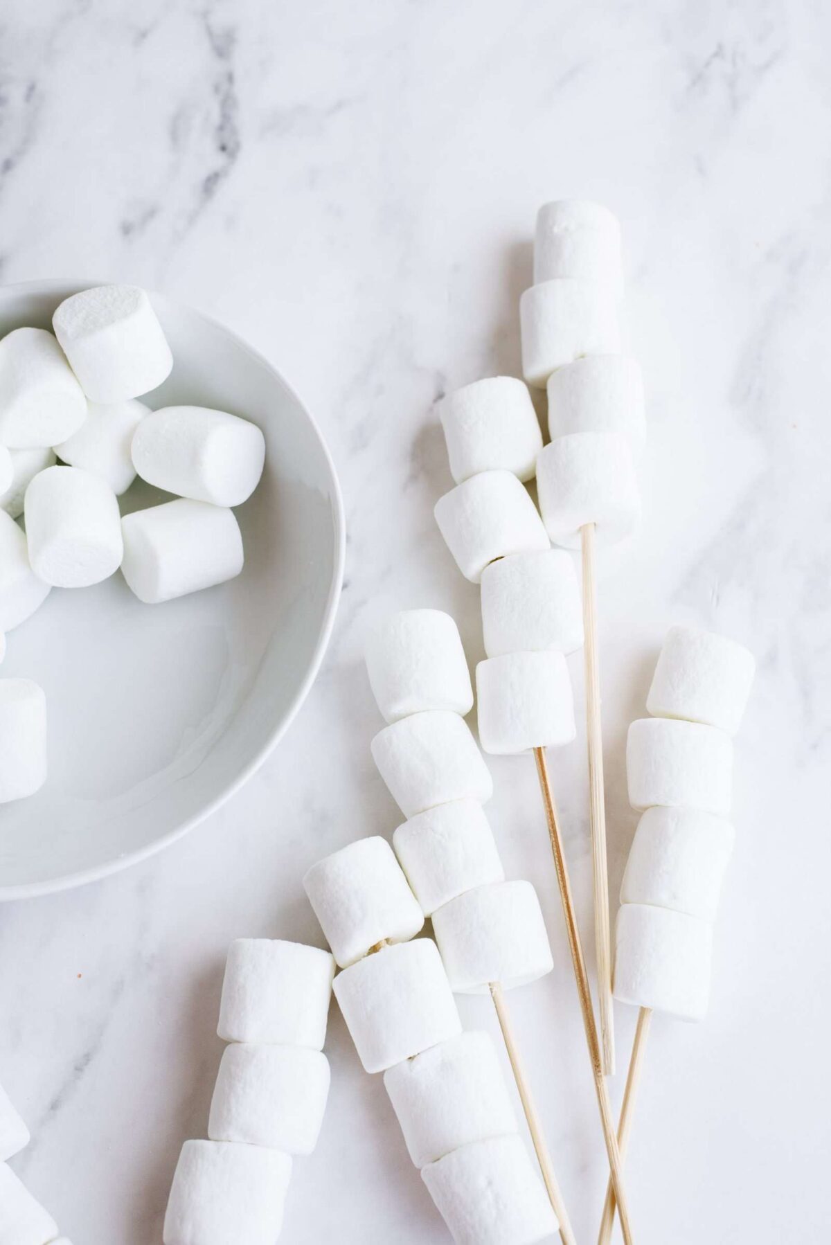 Marshmallows on a plate and some on wooden skewers.