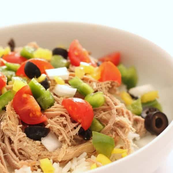 A bowl of kalua pork served over rice, topped with diced tomatoes, green bell peppers, black olives, and chopped white onions.