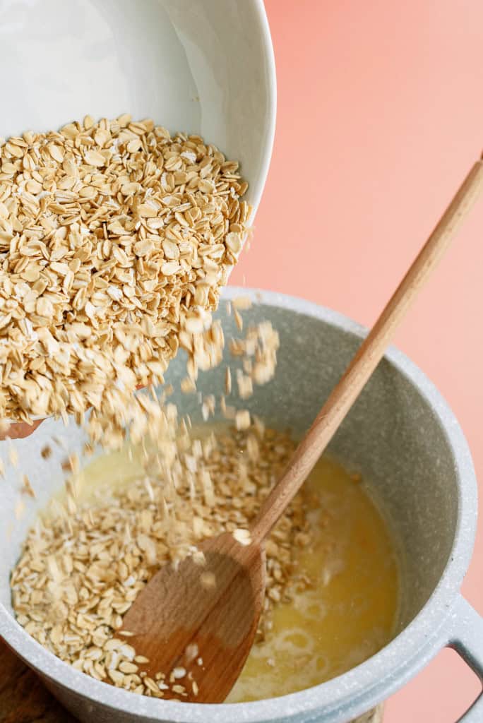 Pouring oats into saucepan with wooden spoon.