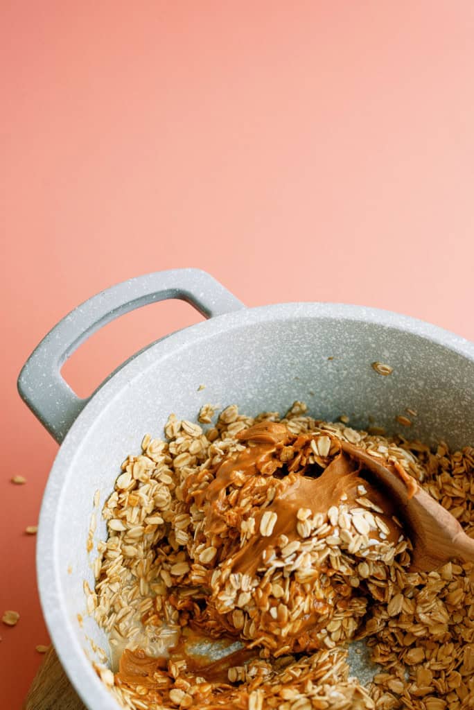 Mixing peanut butter and oats together with wooden spoon in saucepan.