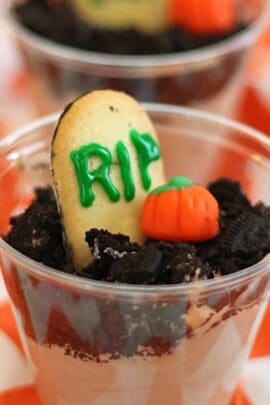 A dessert cup resembling a gravesite, with a cookie "tombstone" labeled "RIP" and a candy pumpkin on top of crumbled chocolate cookies.