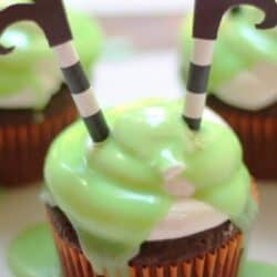 Cupcake with green frosting and two striped paper straws topped with black curled paper cutouts, resembling witches legs.