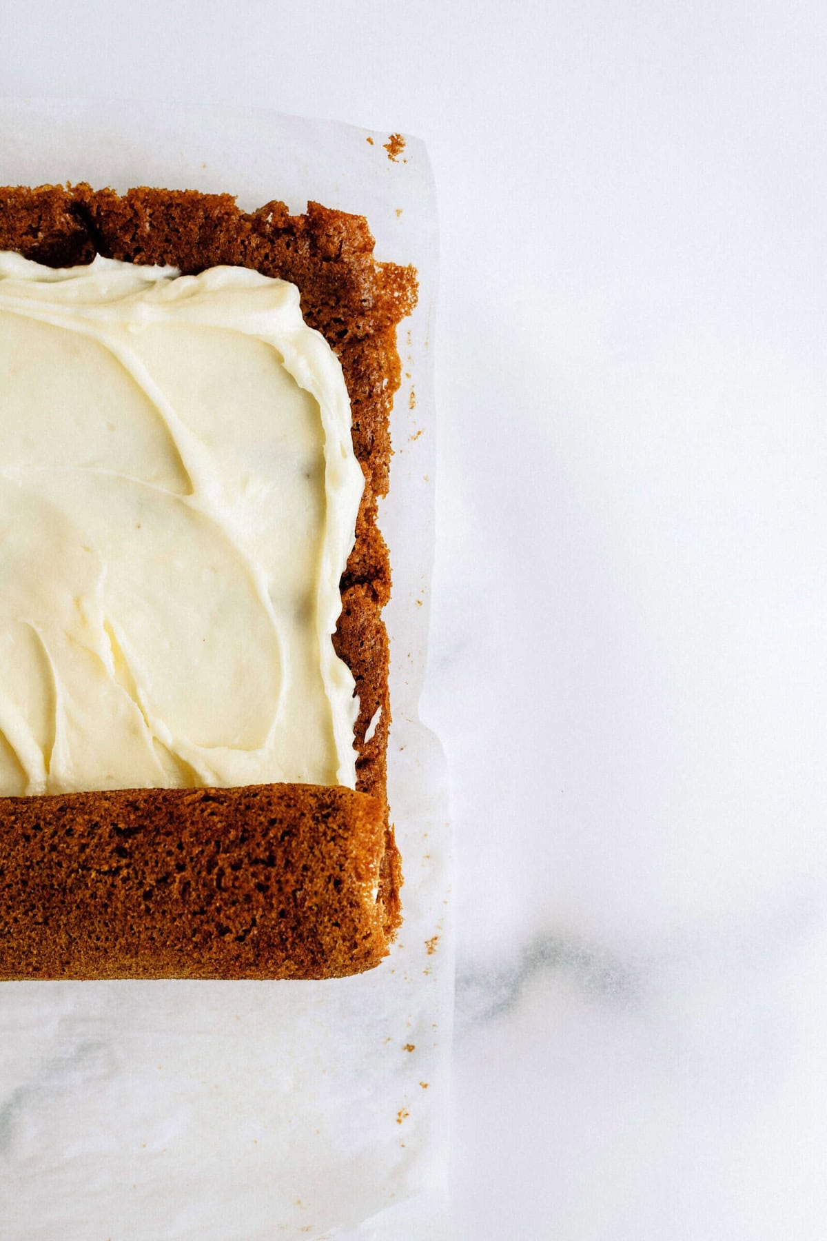 A partially frosted rectangular cake on parchment paper against a white background is seen from the top.