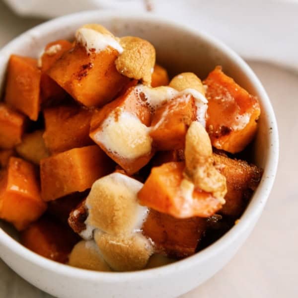 A small white bowl filled with cooked sweet potato cubes topped with melted marshmallows.