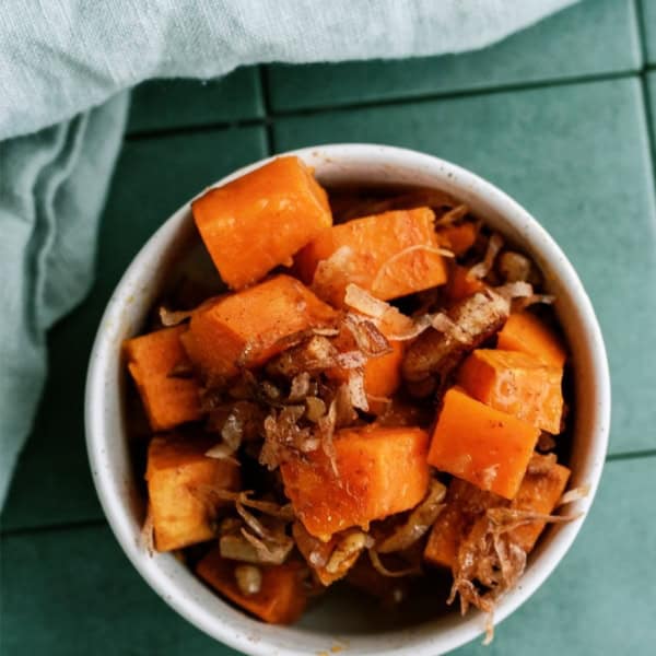 A bowl of cubed sweet potatoes with shredded meat on a green tile surface, accompanied by a light gray cloth napkin.