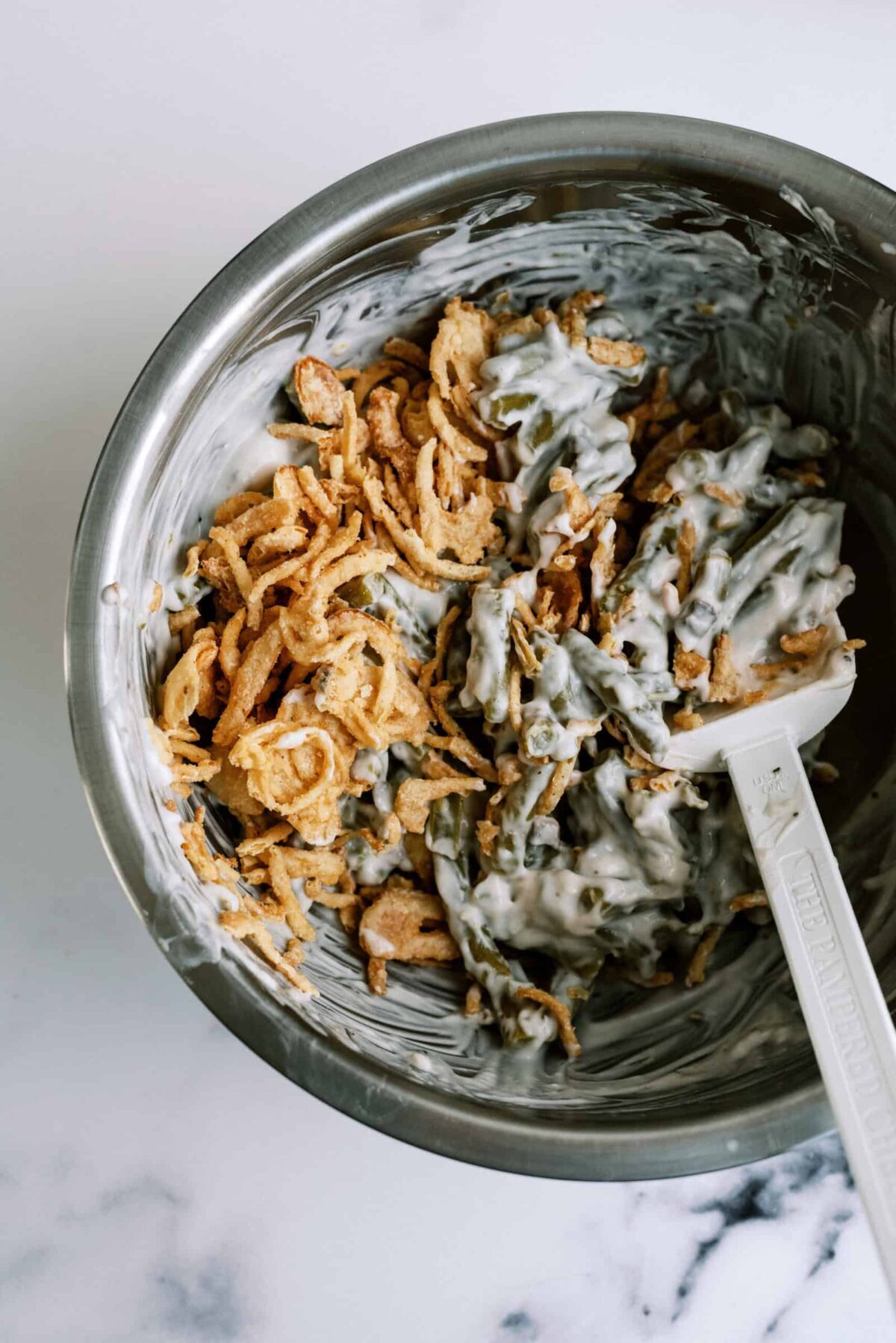 Ingredients needed for Classic Green Bean Casserole mixed together in a mixing bowl with a rubber spatula.