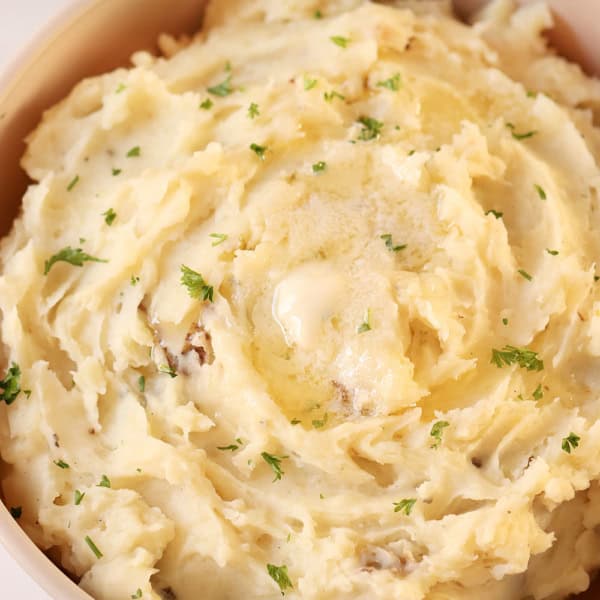 A bowl filled with creamy mashed potatoes, garnished with finely chopped herbs.