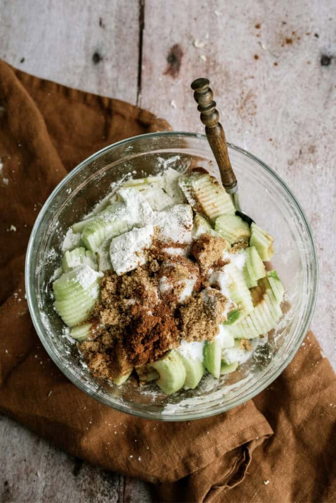 Sliced apples in mixing bowl with seasoning.