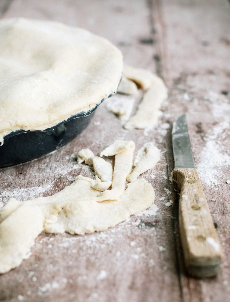 A unbaked apple pie on a counter top with a knife and flour.