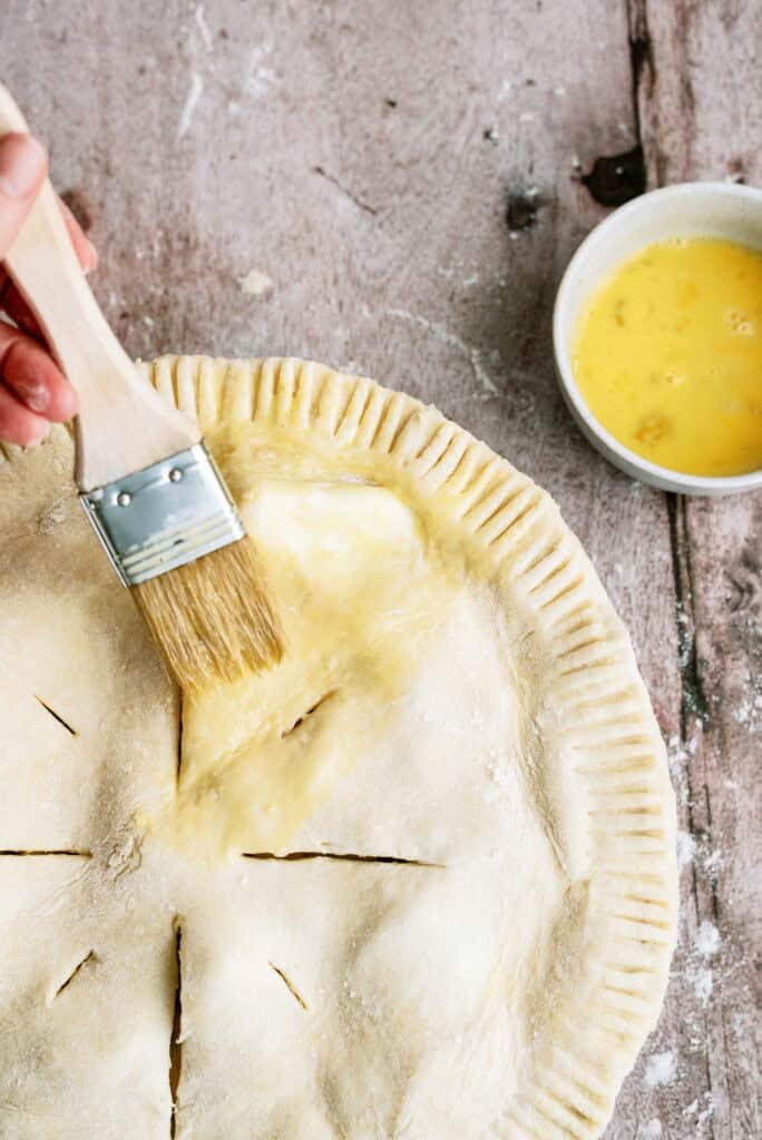 Using a pastry brush to brush an egg wash on top of the pie before baking.