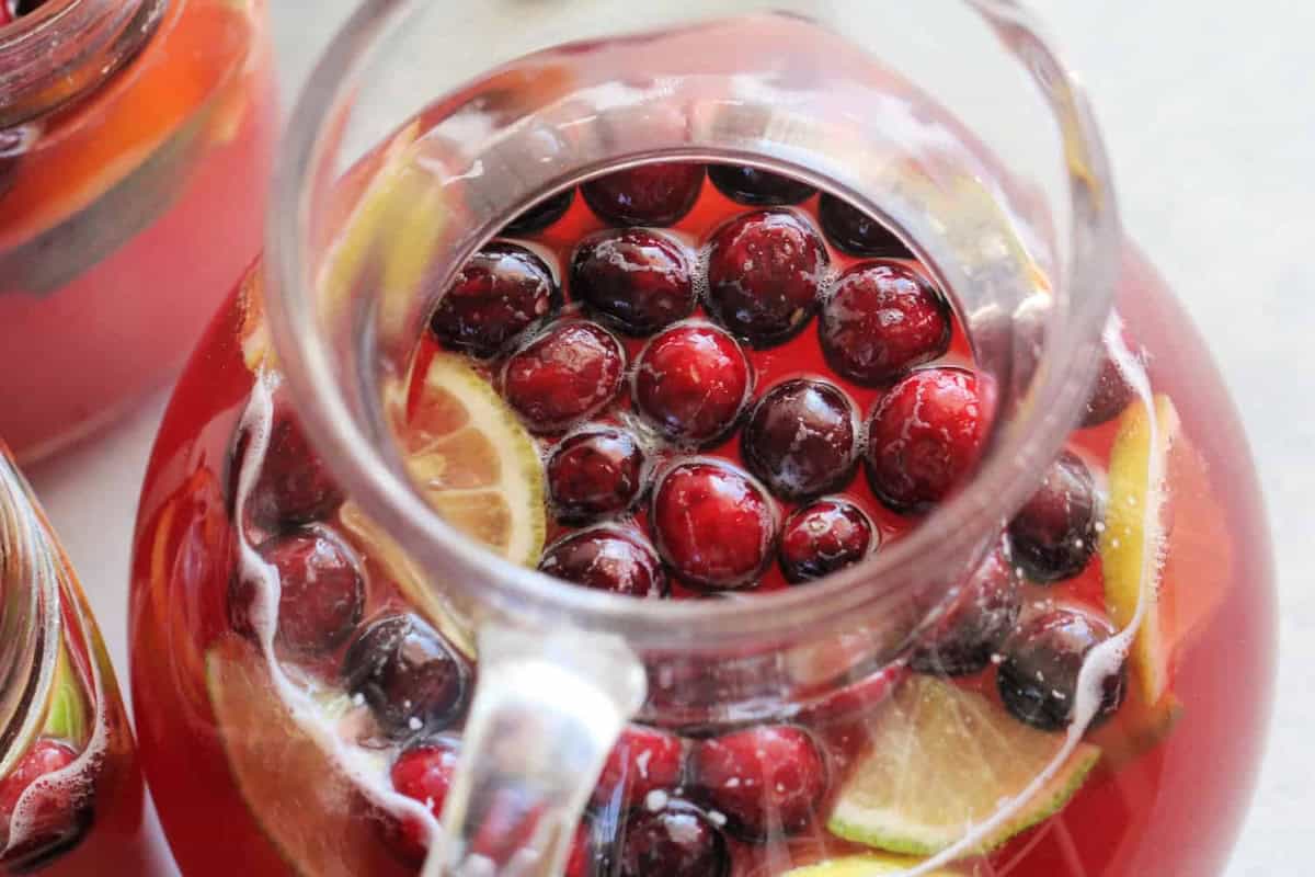 A glass pitcher filled with red liquid, lemon slices, and cranberries.