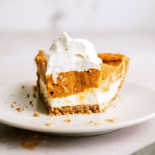 A partially eaten slice of pumpkin pie with whipped cream on top sits on a white plate. Crumbs are scattered around the plate.