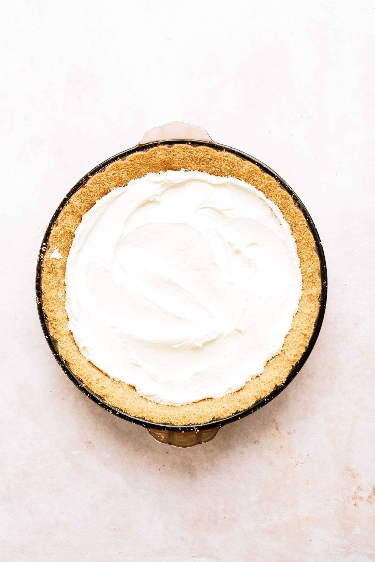 A round pie with a graham cracker crust filled with a smooth, white, creamy filling, placed on a light-colored background.