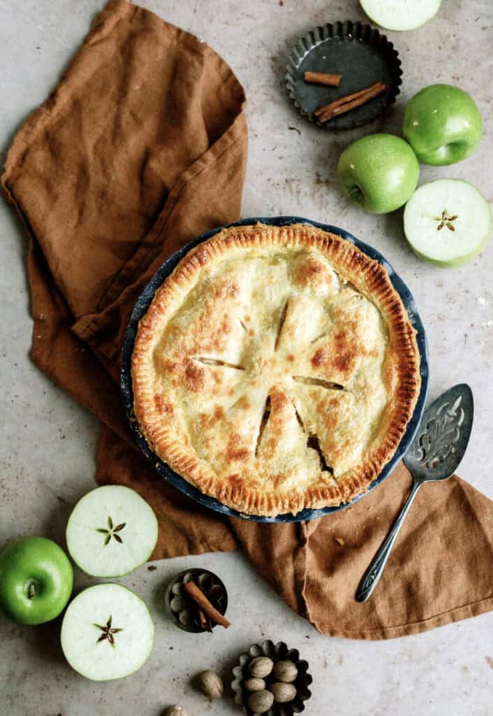 Top view of a fresh baked Classic Apple Pie with other sliced apples around the pie.