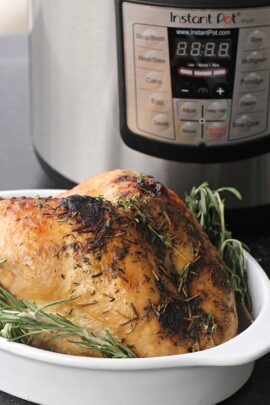 A cooked whole turkey with herbs in a white dish is placed in front of an Instant Pot with a visible control panel.