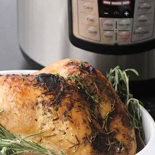 A cooked whole turkey with herbs in a white dish is placed in front of an Instant Pot with a visible control panel.