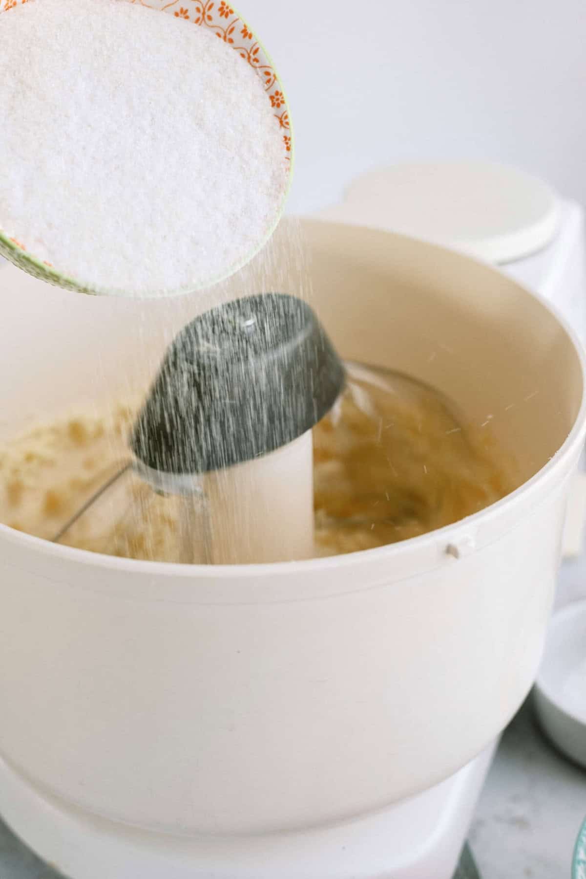 Pouring flour into a stand mixer containing batter.