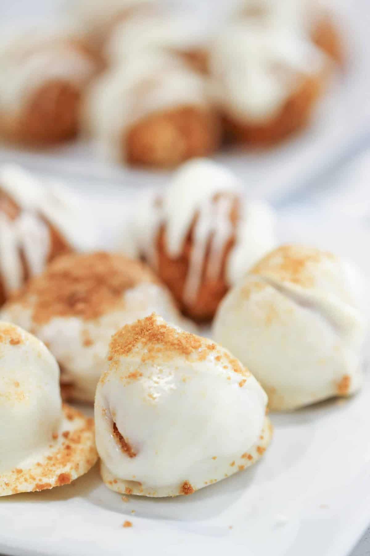 A plate of white chocolate-covered pumpkin spice truffles with a dusting of crumbs, some in focus in the foreground and others blurred in the background.