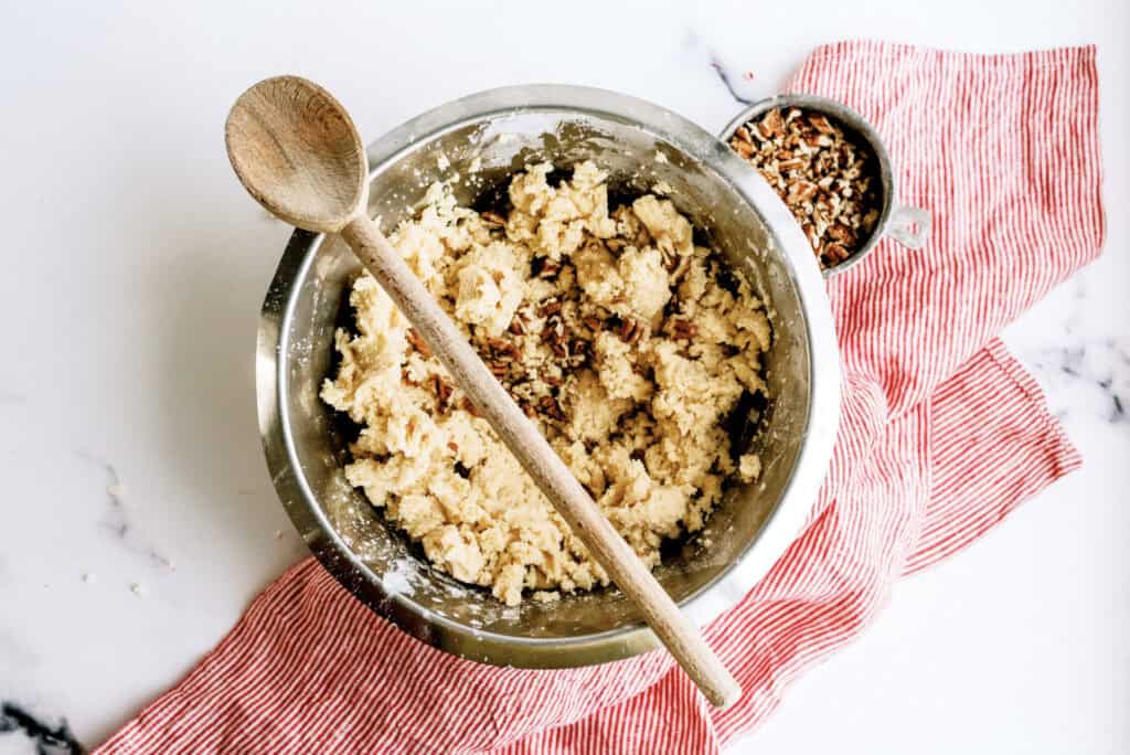 A mixing bowl filled with Peppermint Snowball Cookie dough with a wooden spoon on top.