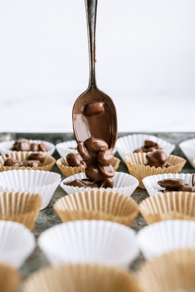 A spoon dropping spoonfuls of the chocolate nut mixture into paper cupcake liners.