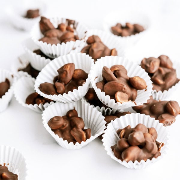 Paper cups filled with clusters of chocolate-covered almonds placed on a white surface.