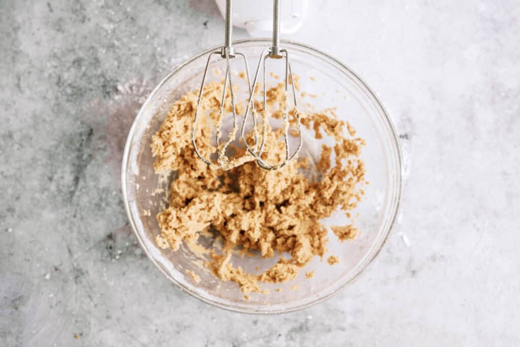 Ingredient in glass mixing bowl mixed together with a hand mixer to create peanut butter dough.