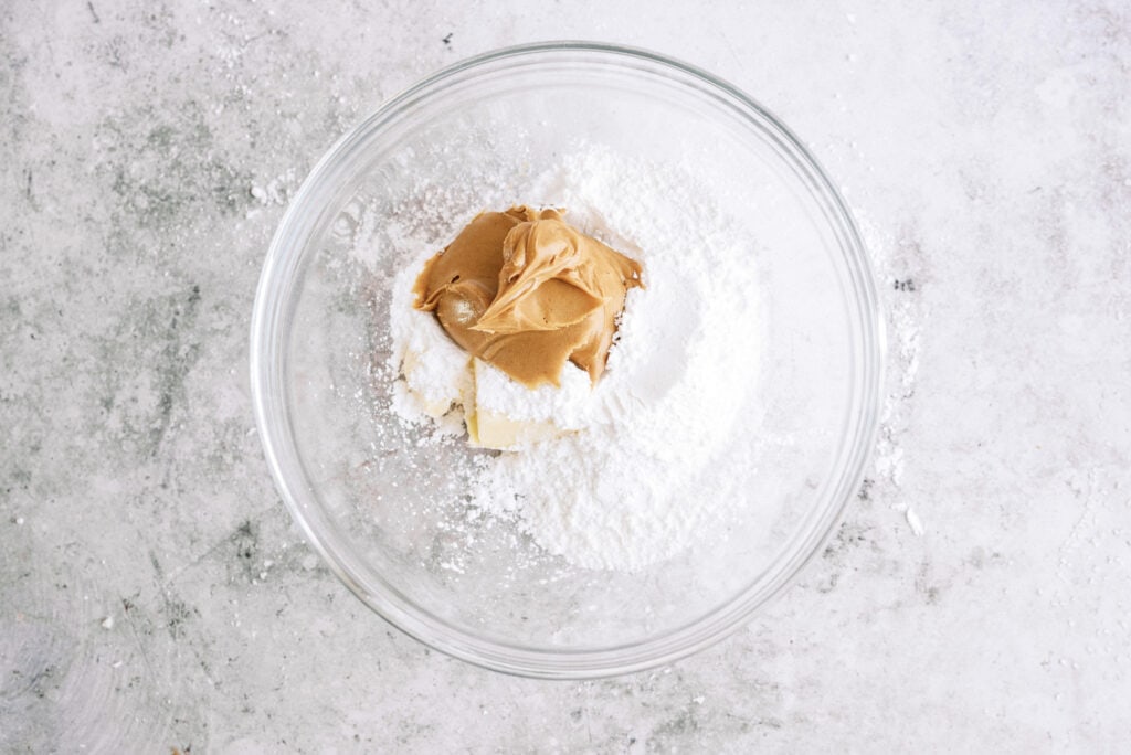 A glass mixing bowl with powdered sugar, peanut butter and butter in it.