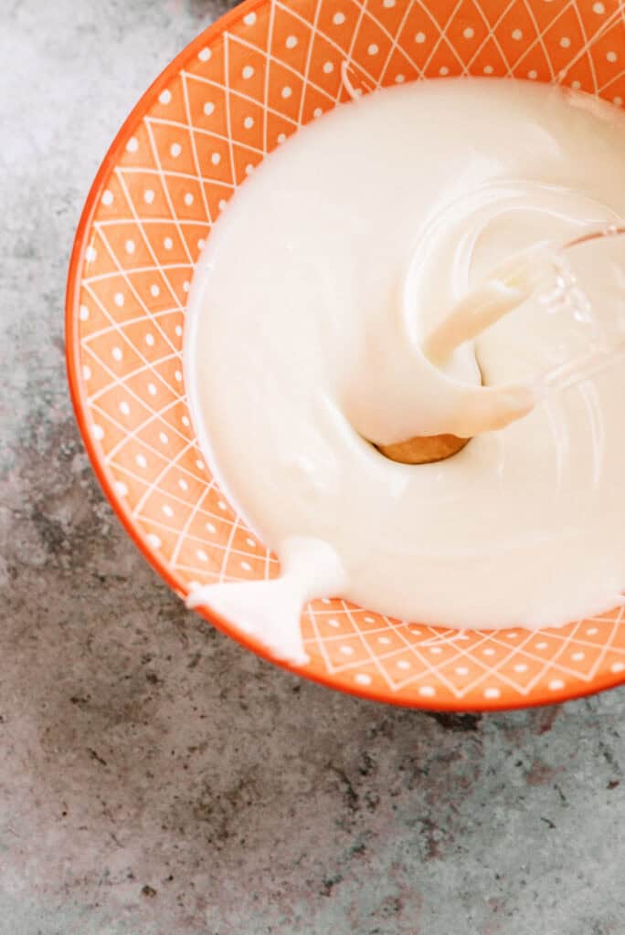 A peanut butter ball dropped into a bowl of melted almond bark with a plastic fork.