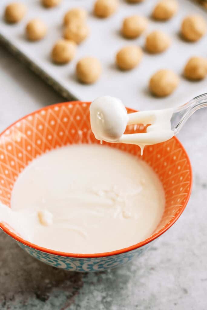 A plastic fork lifting a peanut butter ball covered in white chocolate out of the bowl. 