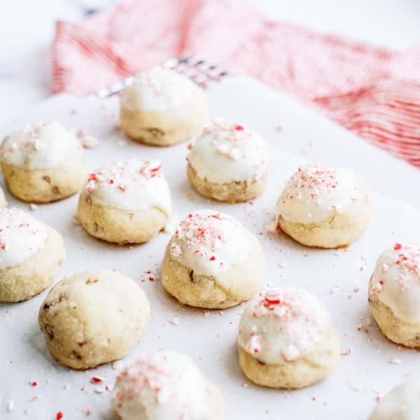 A dozen frosted cookies with white icing and red sprinkles arranged on a white surface with a red and white cloth in the background.