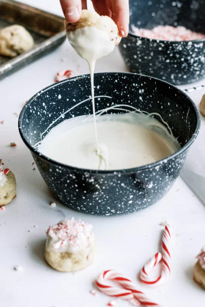 Dipping a cookie ball into a bowl of melted white chocolate.