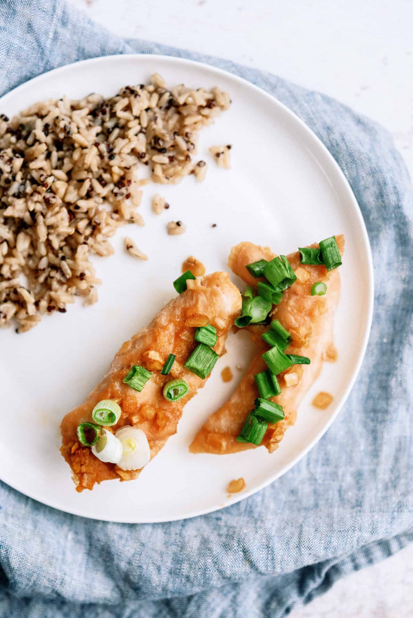 2 Baked Honey Chicken Tenders on a plate with a side of rice. Plate is on top of a blue towel.