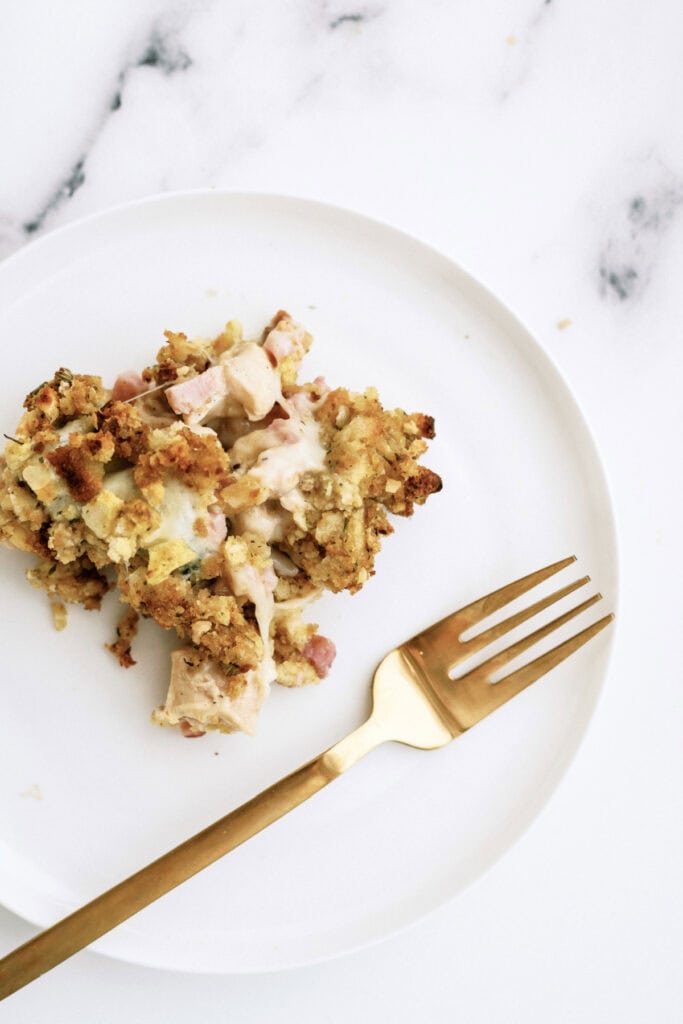 A single serving of a baked casserole with crispy topping is presented on a white plate, accompanied by a gold-colored fork, against a marble backdrop.