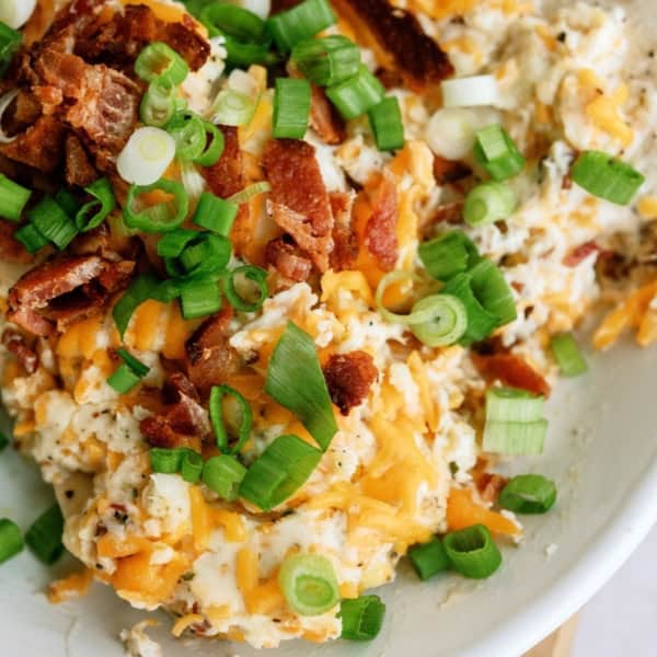 A bowl of loaded mashed potatoes topped with melted cheese, crumbled bacon, and chopped green onions.