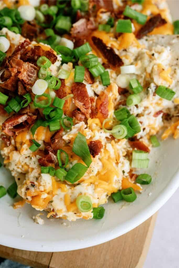 A bowl of loaded mashed potatoes topped with melted cheese, crumbled bacon, and chopped green onions.