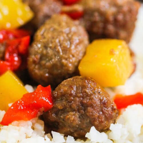 A close-up of a dish featuring meatballs, yellow pineapple chunks, and red bell peppers on a bed of rice.