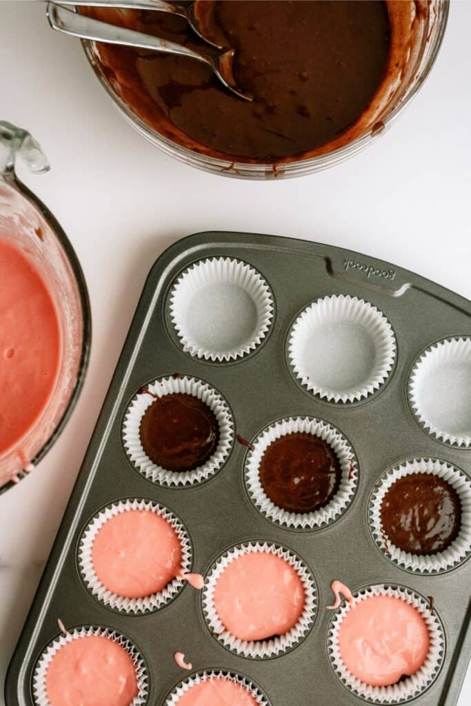 Top view of cupcake pan with strawberry cake batter on top of brownie batter inside the cupcake liners.