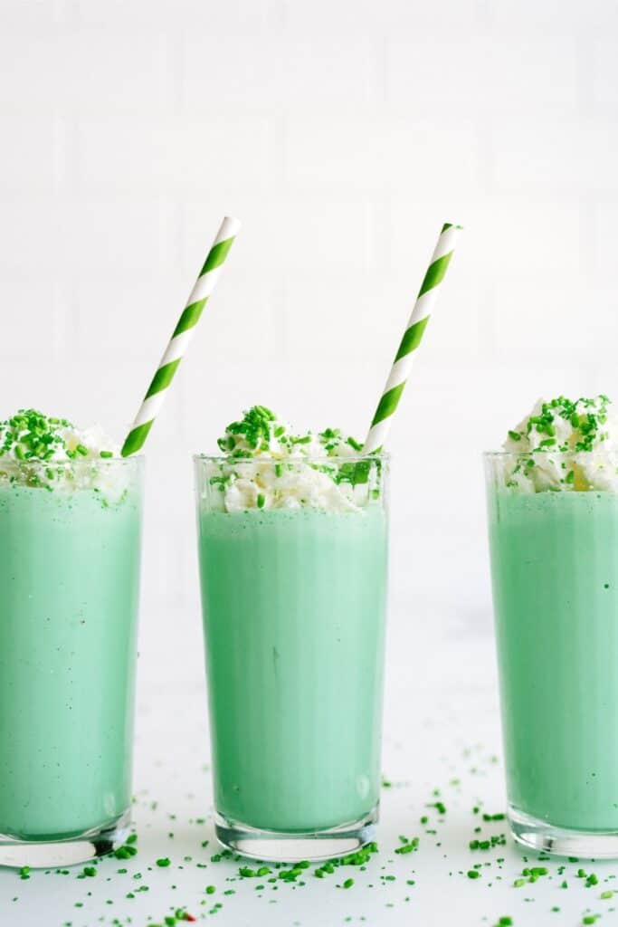 3 Copycat McDonald’s Shamrock Shakes in glasses topped with whip cream and sprinkles with a green striped straw in each glass.